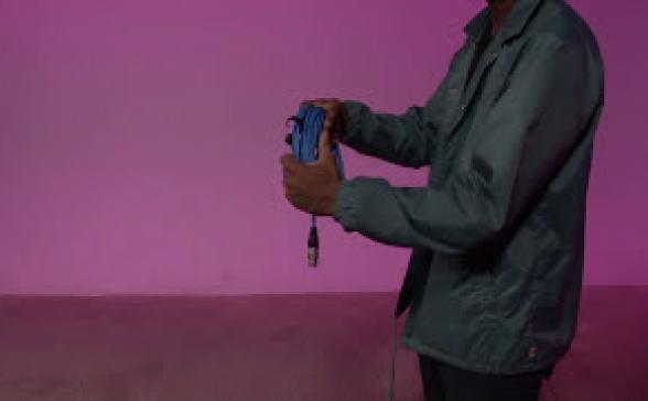still image from the video. A person holding a cable in front of a pink background.