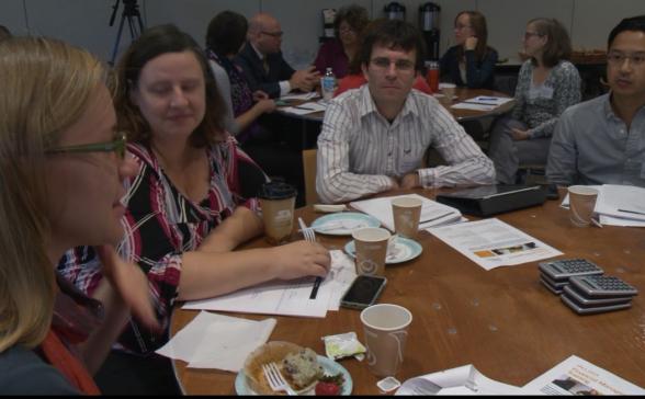 Four people sitting around a table talking. There are several papers on the table.