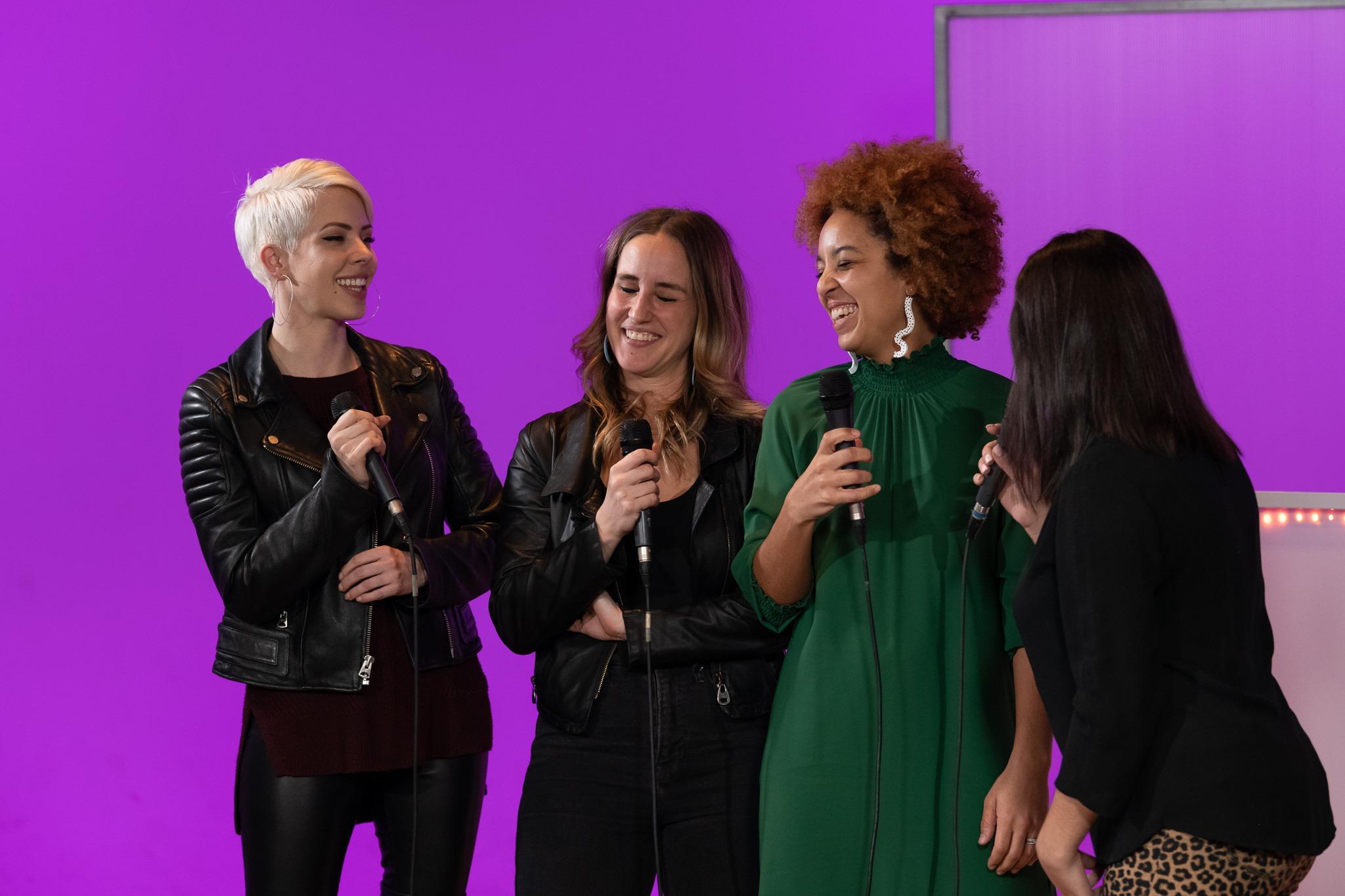 three women with microphones in the SPNN studio with a purple pink background